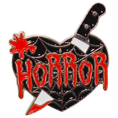 A enamel pin of a black heart with a dagger through it and the word "Horror" printed across it
