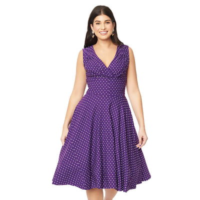 A dark haired smiling model wearing the Unique Vintage Delores Polka Dot Dress - the dress is a cadbury purple with white polka dots