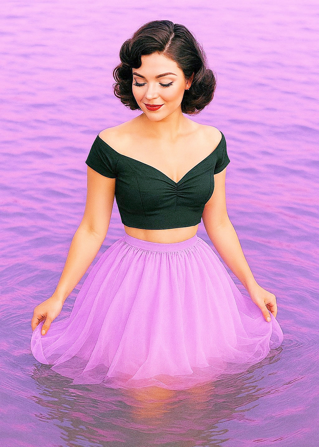 Woman in a black top and purple skirt standing in water with a pinkish-purple gradient background