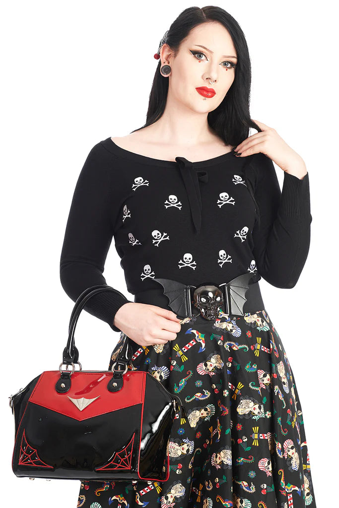 Woman wearing a black top with skull and crossbones design, holding a red and black handbag.