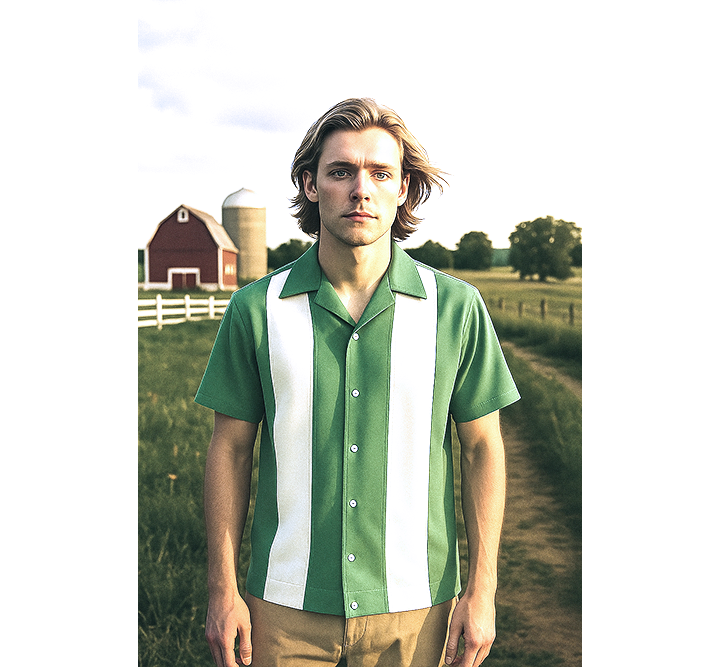 Man wearing a sage and white striped shirt standing in a field with a barn and silo in the background.