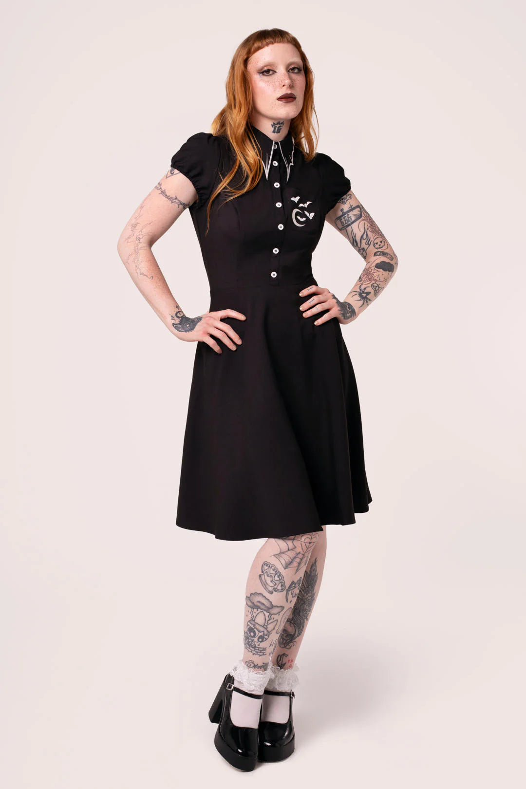 Woman wearing a black dress with tattoos on arms and legs against a white background