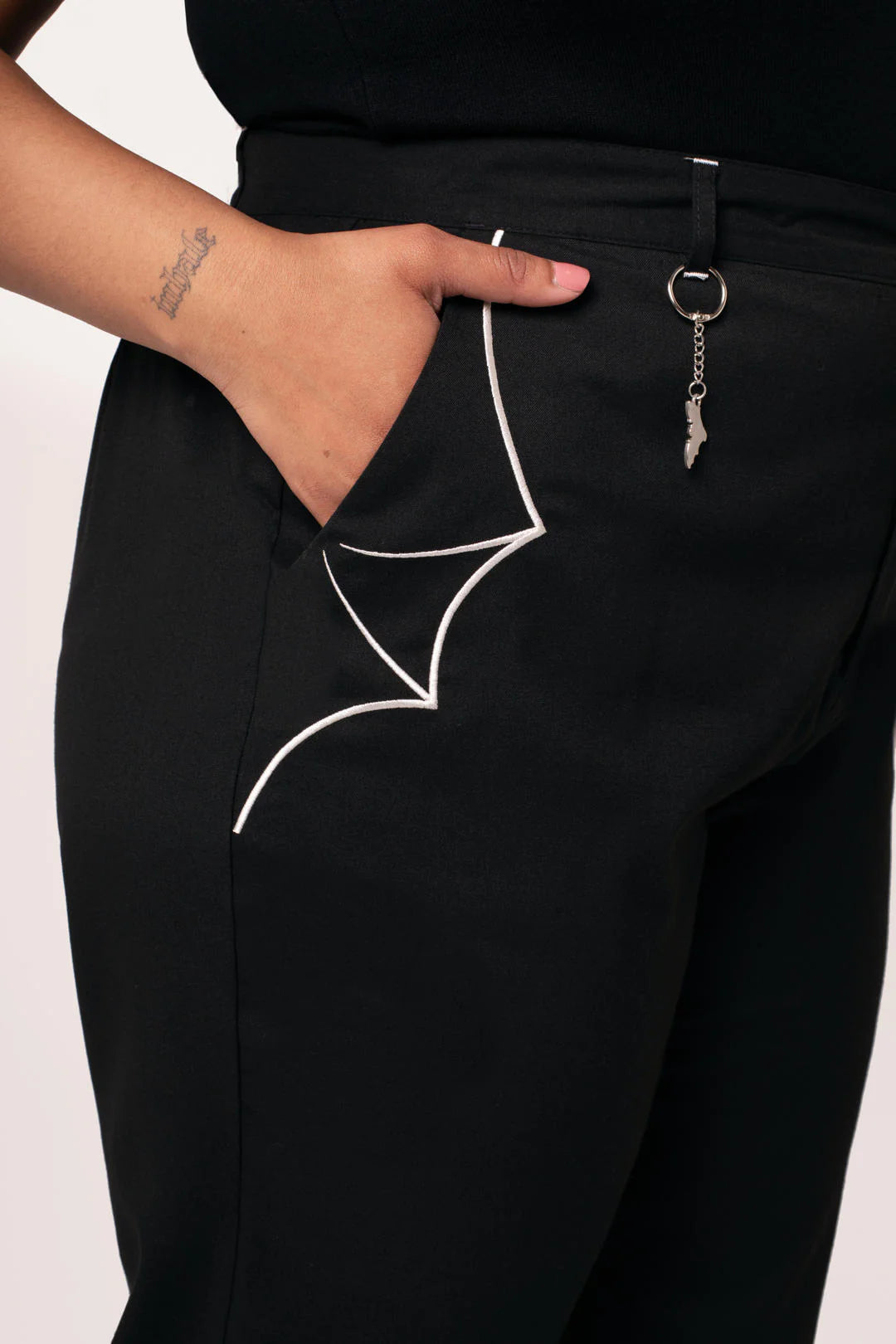 Black pants with white bat wing design and keychain on a plain background