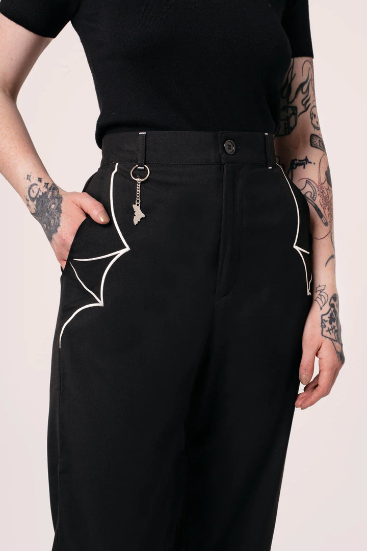 Person wearing black pants with white spider designs on a light pink background