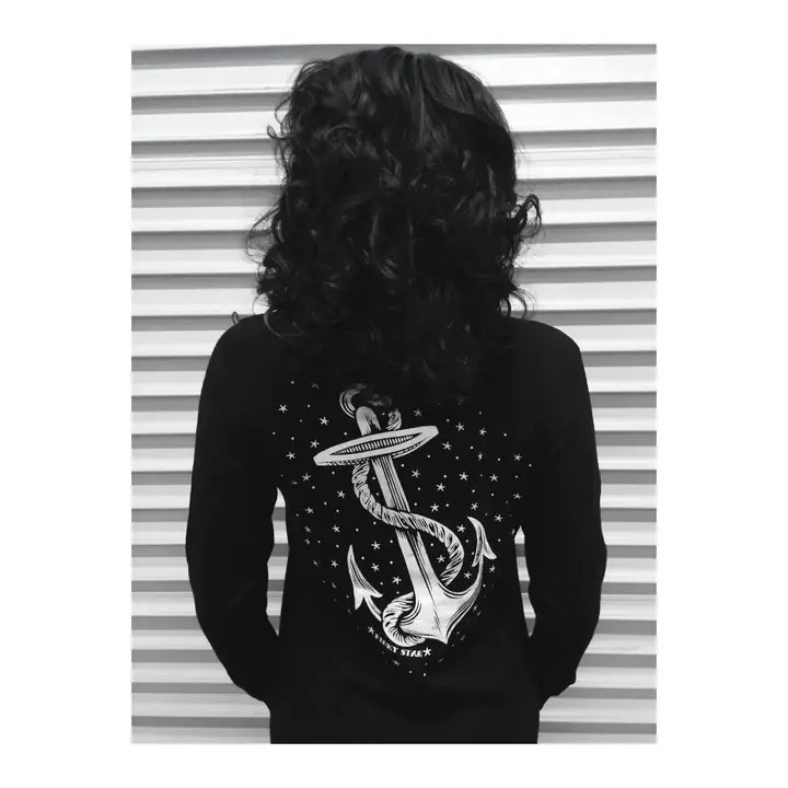 Person wearing a black long-sleeve shirt with an anchor design on the back, standing against a striped background.