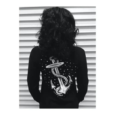 Person wearing a black long-sleeve shirt with an anchor design on the back, standing against a striped background.