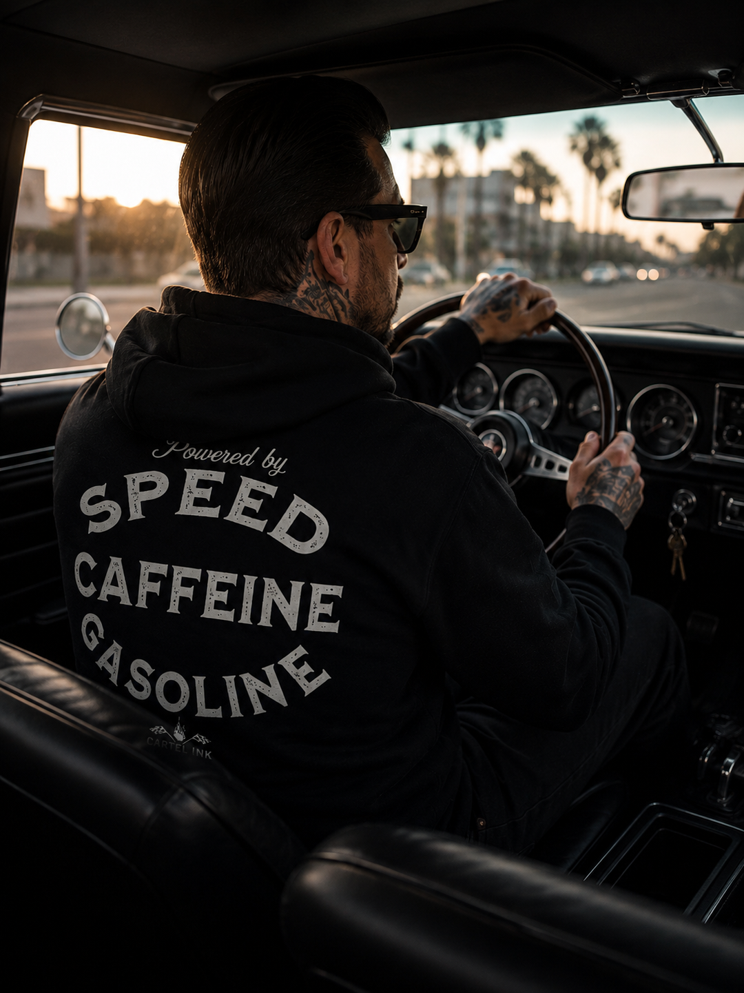 Image from the back seat of a man driving an old car wearing a black hoodie with bold print of Speed, Caffeine and Gasoline