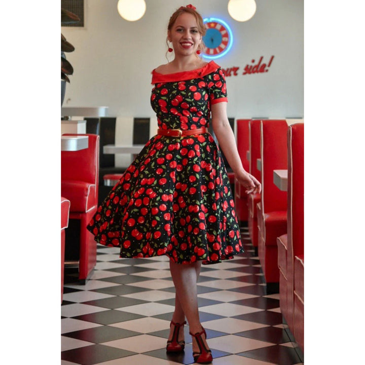 Image of young lady wearing a boat neck black dress with cherry pattern walking through a diner