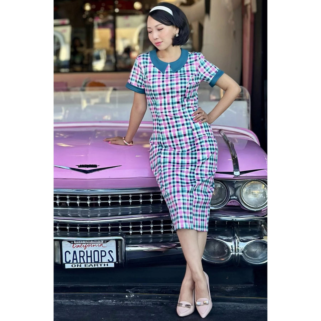 Image of lady wearing a fitted pink, green and white gingham dress posing on a pink convertible car