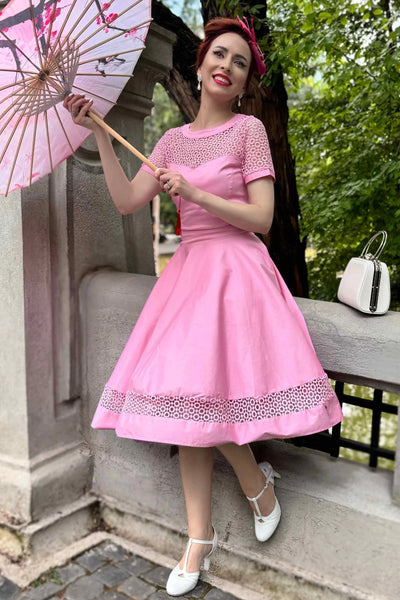 Woman in a pink dress holding a pink umbrella in an outdoor setting