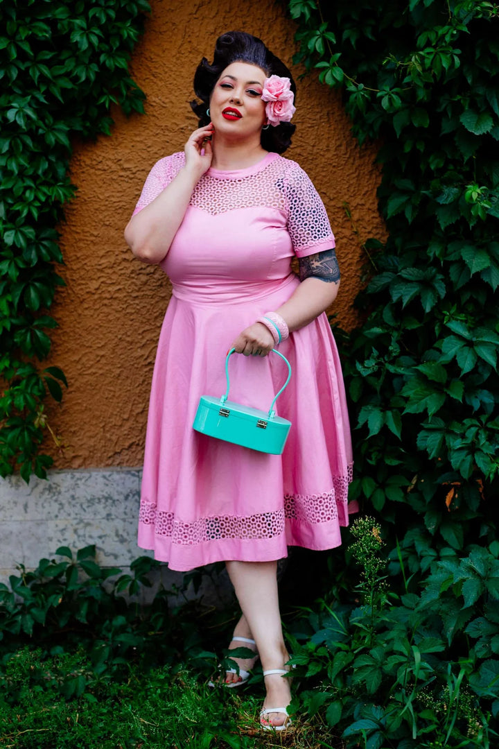Woman in a pink dress holding a turquoise handbag against a green leafy background