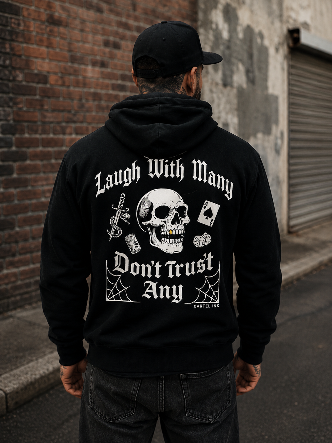 back image of a tattooed man wearing a black hoodie with bold print of "laugh with many dont trust any" and skulls, spider webs and cards