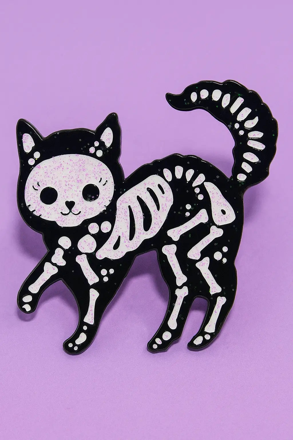 Skeleton cat enamel pin on a purple background.