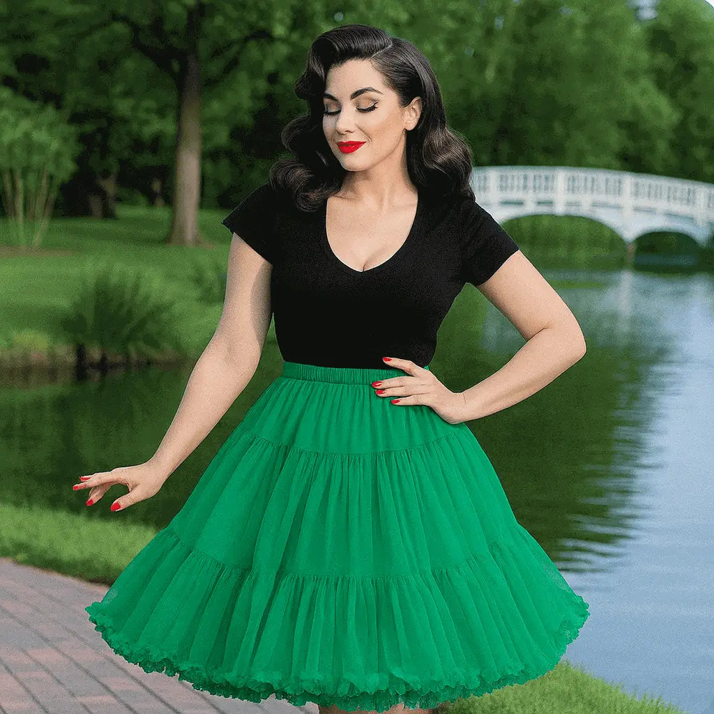Woman wearing a black v-neck top and a voluminous green tiered petticoat skirt standing by a lake with a white bridge.