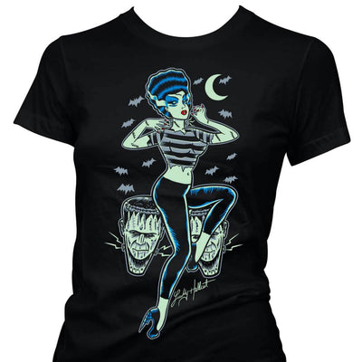 View of Frankenstein Rocker t-shirt. A frankenstein bride sides to the side on two Frrankenstein stools. She has black tight pants, a grey and black ripped t-shirt and Frankenstein bride hair and makeeup. The back ground features a moon and grey bats