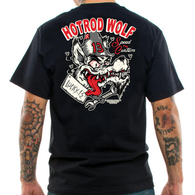 a man with Tattooed arms with his back to us wearing a Lucky 13 t-shirt with a motif  of a hungry looking wolf with its tounge out and text " Hotrod Wolf"